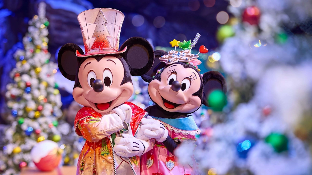Mickey en Minnie Mouse kijken lachend in de camera met kerstboom en kerstballen op de achtergrond tijdens Disney betoverende kerst 2025