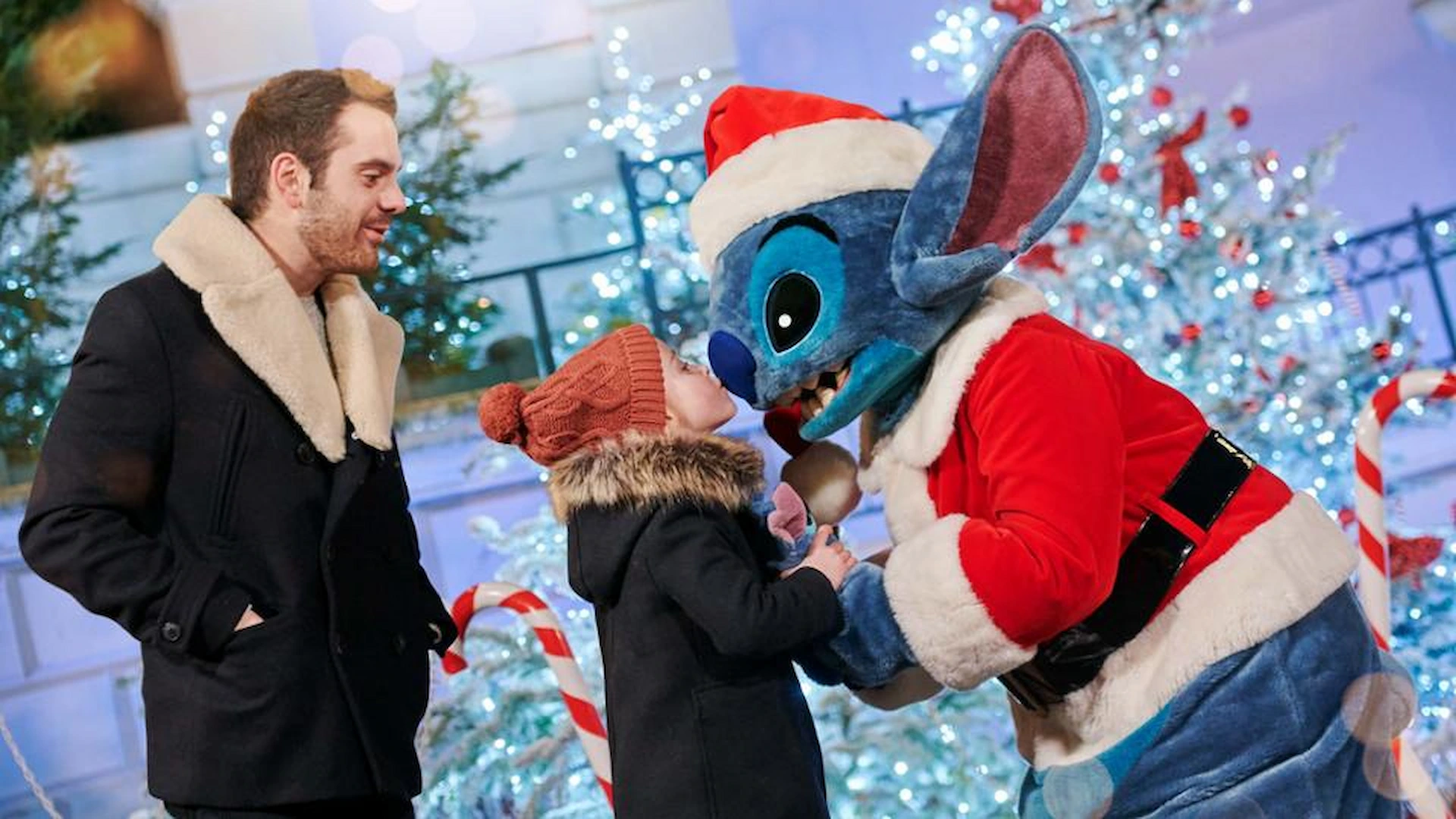 Een kindje geeft Stitch een kusje op zijn neus terwijl de vader toekijkt